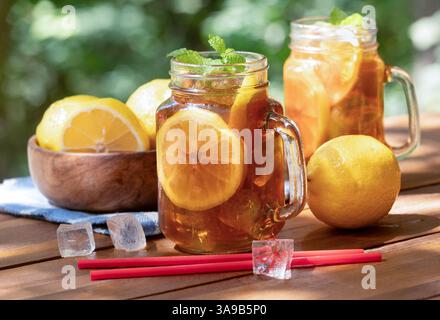 Eistee mit Zitronenscheiben und Minze in Glasbechern im Freien auf Holztisch und Naturhintergrund Stockfoto