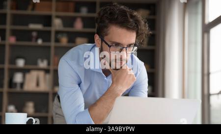 Nachdenklicher männlicher Stand-by-Desk-Reibkin, der auf dem Notebook aussieht Stockfoto