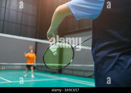 Badminton-Indoor-Sportspieler, der Badminton-Shuttlecock mit Schläger vor dem Netz serviert, und Gegner im Wettkampf Stockfoto
