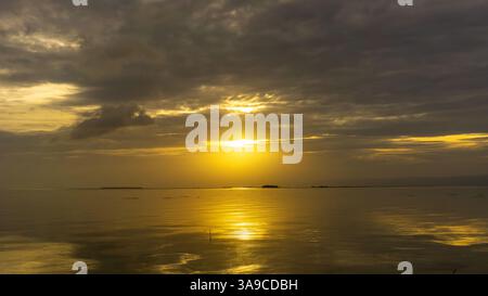Sonnenuntergang über ruhigem Wasser mit Reflexionen und dramatischen Wolken Stockfoto