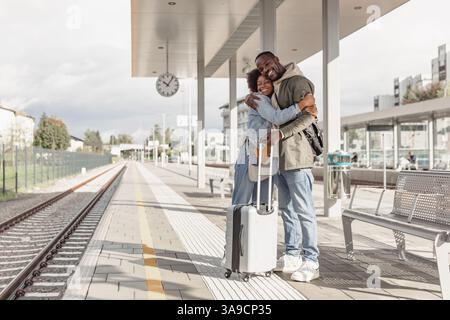 Glückliches, junges afroamerikanisches Paar, das sich an einem Bahnhof umarmt und sich nach einer langen Reise trifft. Reise-, Willkommens- und Liebeskonzepte. Stockfoto