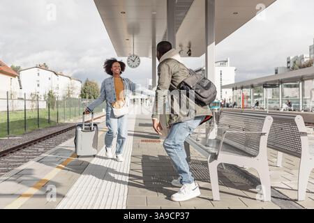 Glückliches, junges afroamerikanisches Paar, das sich an einem Bahnhof umarmt und sich nach einer langen Reise trifft. Reise-, Willkommens- und Liebeskonzepte. Stockfoto