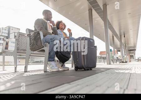 Afroamerikanisches Paar, das mit gepackten Koffern reist und auf einem Bahnsteig auf einen Zug wartet. Stockfoto