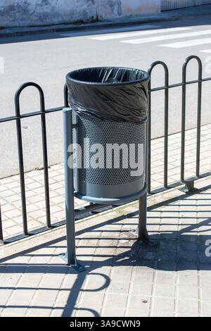 Öffentlicher Müllbehälter aus Metallgeflecht mit schwarzem Müllsack auf einem Stadtbordstein. Stockfoto
