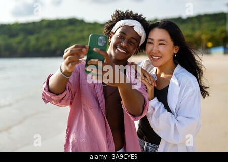 Vielfältige Paare verbunden, mit Technologie und sozialen Medien, während Sie Momente am Strand genießen Stockfoto