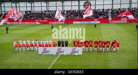 München, Deutschland. 30. März 2025. Begruessung der Zuschauer durch die beiden Teams hinter dem Aufsteller zum Aktionstag Rot gegen Rassismus, dahinter Fahnenschwenker auf dem Rasen vor der Tribuene FC Bayern München Frauen gegen Bayer 04 Leverkusen, Fussball, Google Pixel Frauen-Bundesliga, 18. Spieltag, Saison 2024/2025, 30.03.2025. (DIE DFL-DFB-VORSCHRIFTEN VERBIETEN DIE VERWENDUNG VON FOTOS ALS BILDSEQUENZEN UND/ODER QUASI-VIDEO). Foto: Eibner-Pressefoto/Heike feiner Credit: dpa/Alamy Live News Stockfoto