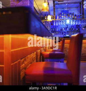 Sitzplätze an einem Bartheken in einer hell beleuchteten Cocktailbar oder einem Nachtclub mit farbenfroher roter und blauer Beleuchtung und Getränken, die in den Regalen auf der Rückseite sichtbar sind Stockfoto