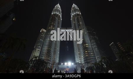 Niedrigwinkelaufnahme von Personen am Boden der beleuchteten Petronas Twin Towers bei Nacht. Kuala Lumpur, Malaysia, Asien Stockfoto