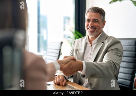 Lächelnder professioneller Geschäftsmann, der den Kunden beim Treffen im Büro mit der Hand schüttelt. Stockfoto