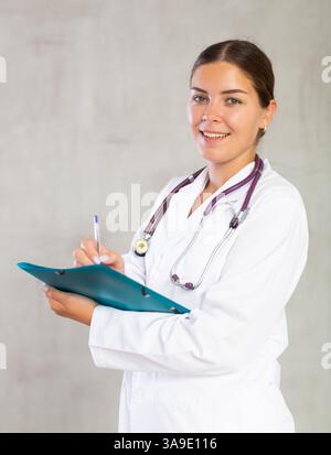 Eine Ärztin macht sich Notizen in Dokumenten, die eine Papiermappe in der Hand haben Stockfoto