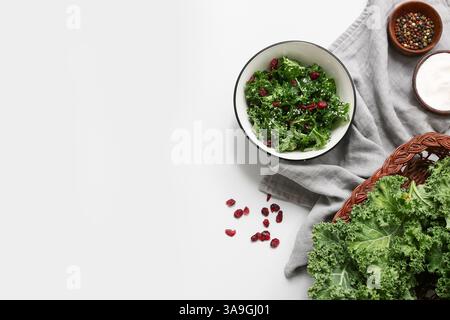 Komposition mit einer Schüssel leckeren Grünkohl-Salat, getrockneten Preiselbeeren und Gewürzen auf hellem Hintergrund Stockfoto