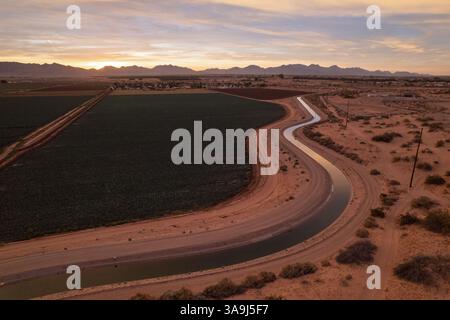 Aus der Vogelperspektive auf Ackerland und Bewässerungskanal bei Sonnenaufgang in der Nähe von Yuma, Arizona, mit Wüstenlandwirtschaft und frühmorgendlichem Licht. Stockfoto