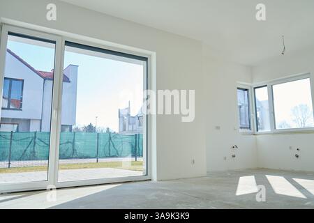 Neues Appartementinnere mit großem Panoramafenster. Modernes, unmöbliertes Zimmer mit Panoramatüren aus Glas und weißen Wänden, das gerade renoviert wird Stockfoto