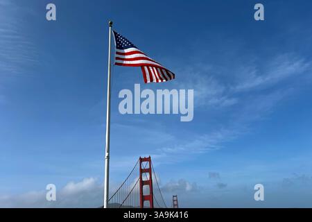 Amerikanische Flagge winkt tagsüber in der Brise nahe der Golden Gate Bridge unter klarem blauen Himmel Stockfoto