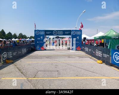 Toronto, ON, Kanada – 14. Juli 2024: Teilnehmer und Mitarbeiter treffen sich in der Ziellinie des Toronto Triathlon Festivals. Branding-Banner und Kanadien Stockfoto