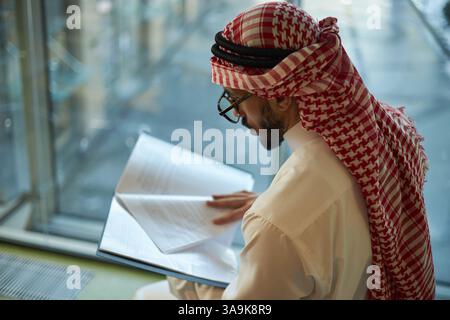 Mittlere Nahaufnahme eines jungen arabischen Geschäftsmannes, der im Büro die Dokumente durchschaut Stockfoto