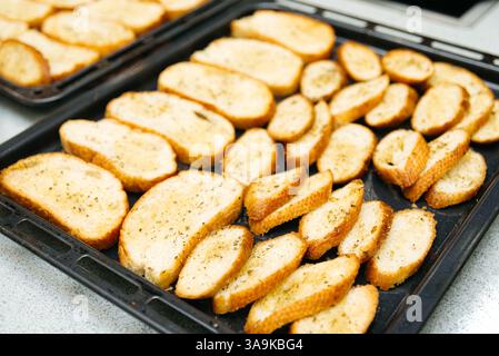 Knusprige, im Ofen gebackene Baguette-Scheiben, mit Kräutern gewürzt, auf Backblechen angeordnet, perfekt für Vorspeisen oder Bruschetta-Basen. Stockfoto
