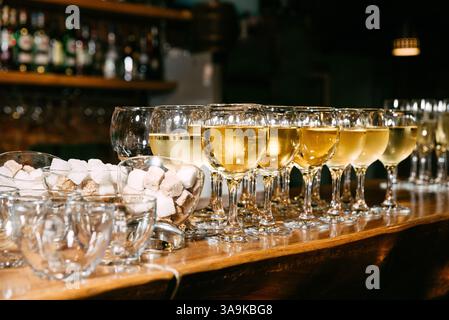 Reihe von Weißweingläsern auf einer Bartheke, klare Schüsseln mit weißen und braunen Zuckerwürfeln und Teetassen. Stockfoto