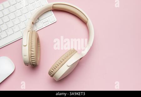 Moderne kabellose Kopfhörer, Tastatur und Computermaus auf rosafarbenem Hintergrund schaffen einen stilvollen und produktiven Arbeitsplatz Stockfoto