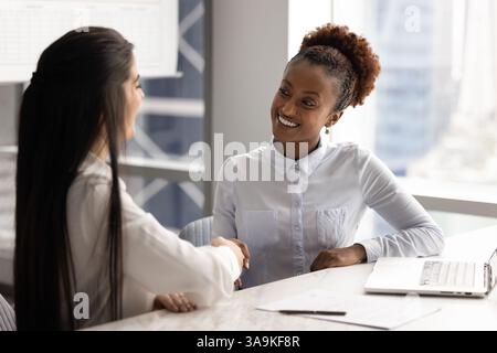 Glückliche, selbstbewusste junge afrikanische Geschäftsfrau, die der Kollegin die Hand schüttelt Stockfoto