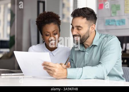 Fröhliche junge afrikanische und kaukasische Manager lesen Papierdokumente Stockfoto