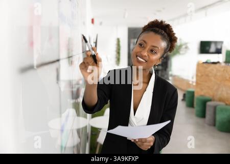 Glückliche schöne schwarze Geschäftsfrau, die auf Kanban-Brett schreibt Stockfoto