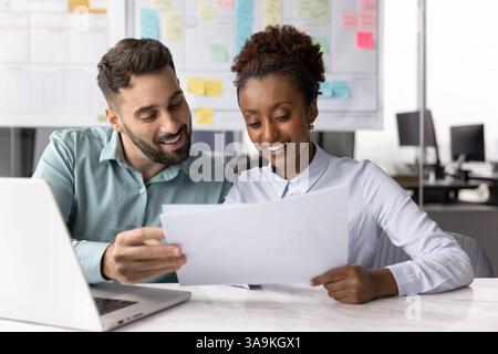 Ein paar positive, multiethnische Geschäftskollegen, die Finanzberichte auf Papier analysieren Stockfoto