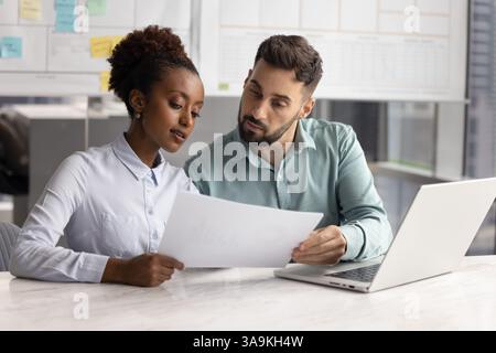 Zwei ernsthafte, fokussierte, multiethnische Kollegen, die finanzielle Rechtsdokumente überprüfen Stockfoto