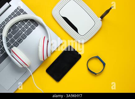 Moderne digitale Gadgets und Zubehör. Laptop, Smartphone, intelligentes Armband, Kopfhörer, wlan-Router auf gelbem Hintergrund. Draufsicht. Stockfoto