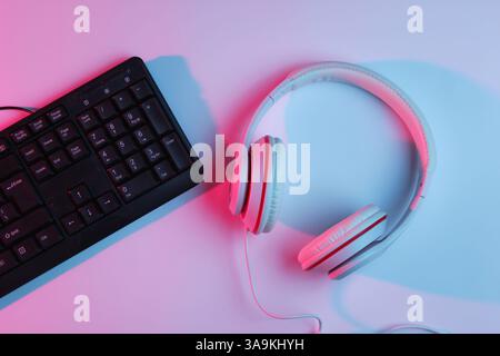 Spielgeräte. Tastatur und Kopfhörer mit Neonverlauf rosa-blauem Licht. Musikkonzept. Computerspielwettbewerb. Draufsicht Stockfoto