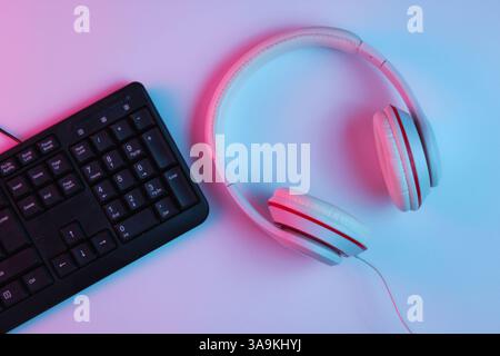 Spielgeräte. Tastatur und Kopfhörer mit Neonverlauf rosa-blauem Licht. Musikkonzept. Computerspielwettbewerb. Draufsicht Stockfoto