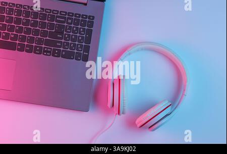 Spielgeräte. Laptop und Kopfhörer mit Neonverlauf Rosa-Blau-Licht. Musikkonzept. Computerspielwettbewerb. Draufsicht Stockfoto