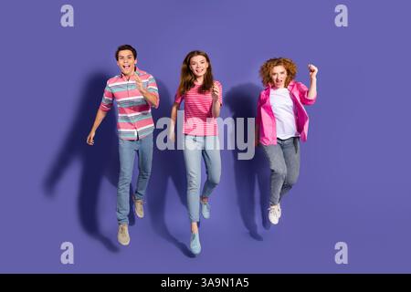 Gruppe energiegeladener junger Freunde in legeren Outfits, die vor einem violetten Hintergrund springen und Freude und Aufregung ausdrücken Stockfoto