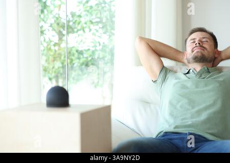 Mann, der zu Hause mit intelligentem Lautsprecher auf einem Sofa sitzt Stockfoto