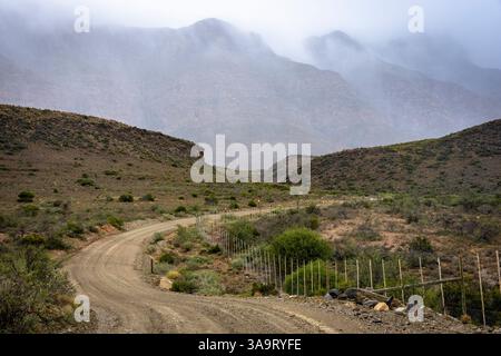 Schotterstraße entlang der Hänge der Swartberg Mountains bei wildem und windigem, bewölktem Wetter. In der Nähe von Klaarstroom und de Rust. Westkap. Südafrika Stockfoto