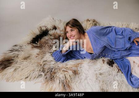 Frau in fließendem Kleid, die auf einem strukturierten Pelzteppich liegt Stockfoto