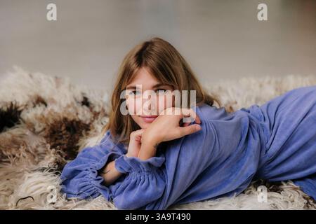 Frau in fließendem Kleid, die auf einem strukturierten Pelzteppich liegt Stockfoto