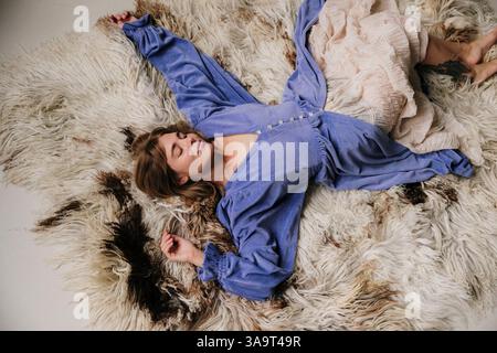 Frau in fließendem Kleid, die auf einem strukturierten Pelzteppich liegt Stockfoto