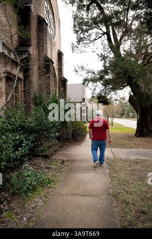 Person in rotem Hemd, die an einer historischen Backsteinkirche auf einem Bürgersteig vorbeiläuft Stockfoto