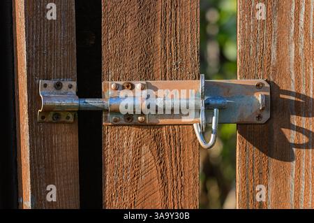 Nahaufnahme eines rostigen Metallriegels an einem hölzernen Gartentor mit verwitterten Texturen und sicherem Verschluss. Erfasst Details von alterndem Metall und rauem Holz Stockfoto
