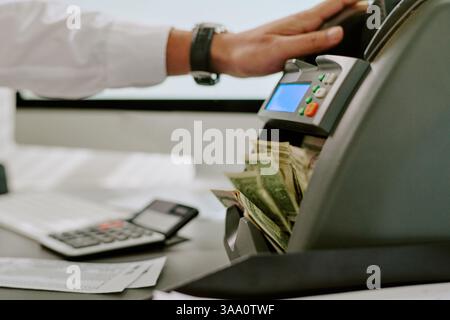 Nahaufnahme einer Person, die die elektronische Kasse anpasst, mit Rechner und Bargeld neben der Geschäftsumgebung, Szene, die den Finanztransaktionsprozess in einem modernen Arbeitsplatz darstellt Stockfoto
