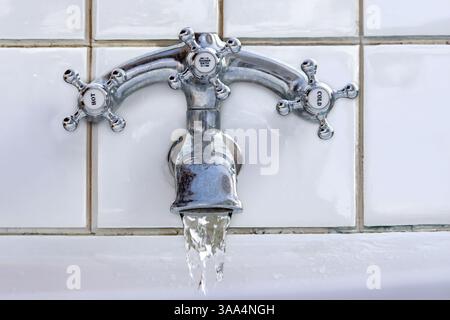 Chrom-Wasserhahn im Retro-Stil mit fließendem Wasser an einer weißen gefliesten Wand Stockfoto