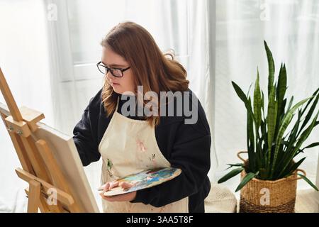 Eine junge Frau mit Down-Syndrom zeigt ihre Kunst auf Leinwand zu Hause. Stockfoto
