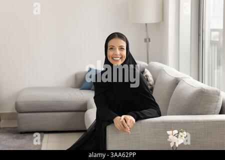 Frau aus dem Nahen Osten, gekleidet in traditioneller Abaya, die auf dem Sofa ruht Stockfoto
