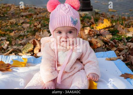 Niedliches Baby in rosafarbenem Outfit, das im Herbst Blätter im Freien genießt. Stockfoto