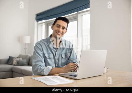 Der Mann sitzt am Schreibtisch mit Laptop, lächelt und blickt in die Kamera Stockfoto