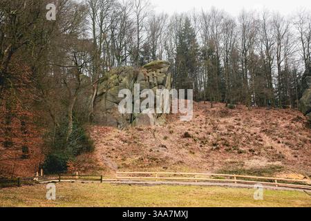 Ein großer Felsen liegt auf einem Hügel neben einem Zaun in Deutschland. Der Hügel ist mit Bäumen und Gras bedeckt Stockfoto