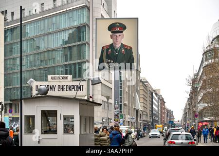Berlin, Deutschland - 27. März 2025: Blick auf den historischen Checkpoint Charlie in Berlin mit Kontrollhäuschen, Porträt eines Soldaten und vielen Passanten entlang der Straße *** Blick auf den historischen Checkpoint Charlie in Berlin mit Kontrollhäuschen, Porträt eines Soldaten und vielen Passanten entlang der Straße Stockfoto