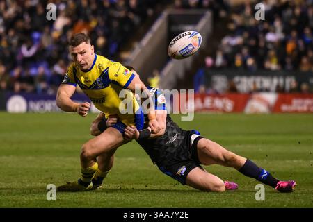 WARRINGTON, ENGLAND – 28. MÄRZ 2025: George Williams von Warrington Wolves verlässt den Tod trotz des Tackles von Lachie Miller aus Leeds Rhinos duri Stockfoto