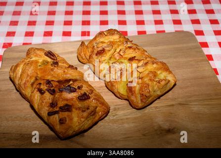 Köstliche Blätterteiggebäck gefüllt mit Nüssen und Früchten ruhen auf einem Holzbrett. Die rot-weiß karierte Tischdecke verleiht dem Café einen charmanten Touch Stockfoto